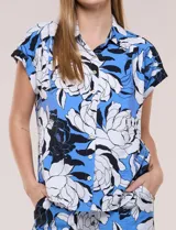 Camisa de manga corta confeccionada en rayón y poliéster, con estampado floral en tonos azules, negros y blancos, cuello camisero clásico y cierre frontal de botones.