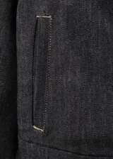 Chaqueta de denim en color negro, de corte clásico con cierre frontal de botones metálicos, cuello camisero y bolsillos con solapa en el pecho.