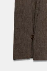 Pantalón de tiro medio con pernera recta y amplia, confeccionado en tejido con textura. Presenta una pieza superpuesta tipo pañuelo anudada en la cintura y bajo ajustable con botón.