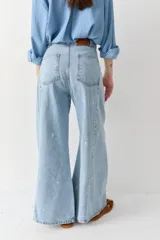Jean de corte wide leg y tiro alto, confeccionado en denim de lavado claro. Presenta un diseño con costuras verticales frontales y un sutil estampado de figuras deportivas pequeñas distribuidas por toda la prenda.