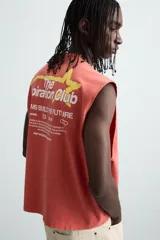 Camiseta tank cropped fit color ladrillo, con cuello redondo y sisa. Estampado frontal y trasero con gráficos y textos en color amarillo. Efecto lavado.