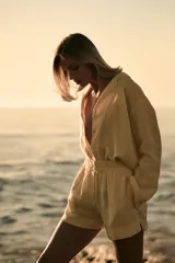 Short de tiro medio de lino 100%, color amarillo claro. Presenta cintura elástica, cierre frontal con botones y bolsillos laterales ocultos en costura y de plastrón en la espalda. El bajo tiene aberturas laterales.