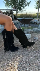 Botas de caña media confeccionadas en gamuza, con diseño holgado y detalle de flecos laterales con cadena metálica. Cuentan con suela plana y estilo western.