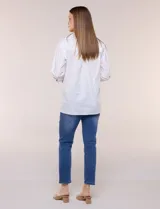 Camisa de silueta holgada y largo extendido, confeccionada en poplín elástico de color blanco. Presenta cuello solapa abierto en V con cartera frontal de abotonadura oculta, hombros caídos y mangas tres cuartos. Cuenta con espalda con canesú, pliegue central y ruedo recto con pequeñas aberturas laterales.