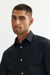 Camisa de tela azul marino con tratamiento de fácil planchado. Modelo Slim Fit con cuello inglés, tapeta clásica, canesú en la espalda, mangas largas con tapeta y botón, y puños ajustables con botón. Bajo ligeramente redondeado.