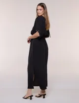 Vestido largo amarillo de corte fluido con escote en V, mangas cortas amplias y apliques de tachas en el escote y puños. Posee cintura elastizada fruncida y falda larga con tajos laterales en el ruedo.