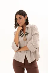 Camisa de textura plisada en color beige, con cuello clásico, cierre frontal de botones y mangas tres cuartos con puños vueltos.