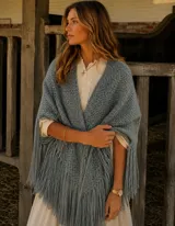 Ruana de lana merino en color gris azulado, con tejido de punto texturizado y flecos largos en los bordes.