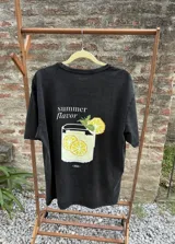 Remera de algodón color negro con efecto lavado, de manga corta y cuello redondo. Presenta un estampado frontal con estilo pixel art de un trago con rodajas de limón y el texto 'summer flavor'.