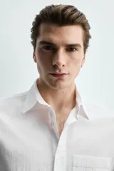 Camisa de corte regular fit color blanco, confeccionada en tejido de algodón con efecto arrugado, con cuello solapa, manga larga, puños abotonados y un bolsillo de parche en el pecho.