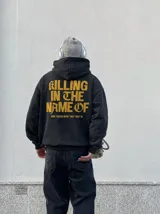 Hoodie canguro con cierre frontal, color negro con efecto acid wash, con capucha y bolsillos tipo canguro. Presenta el texto estampado en amarillo "Now You Do What They Told Ya" en el pecho.
