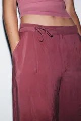 Pantalón de tiro alto color bordó, de corte ancho y pierna recta, con pinzas frontales y lazada ajustable en la cintura. El tejido presenta un acabado satinado o ligeramente arrugado.