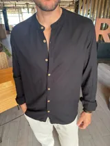 Camisa de manga larga color negro con cuello mao y cierre frontal de botones de madera. Confeccionada en tejido símil lino.