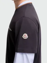 Remera de manga corta color negro con bordado Moncler Archive en el pecho, diseñada con un efecto de capas que incluye mangas largas de camisa en color celeste y cuello en tono marrón.