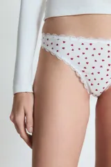 Pack de tres bombachas tipo colaless con terminaciones de encaje. Incluye una unidad negra con un corazón bordado, una unidad blanca con estampado de corazones rojos y una unidad beige con un corazón bordado.