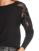 Buzo de tejido acanalado color negro con cuello a la base y mangas largas. Presenta detalles decorativos en los hombros con aplicaciones de microtul bordado y lentejuelas.