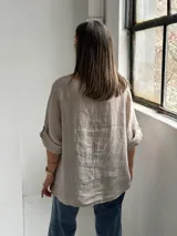 Blusa de lino color beige, de corte holgado, cuello redondo y mangas 3/4 con presillas y botones para sujetar el largo.