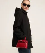 Saco corto negro de polivelour con capucha, cuello alto con cremallera, abotonado delantero cruzado, bolsillos delanteros y mangas largas.