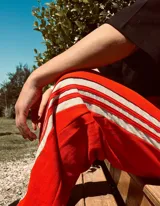 Pantalón deportivo color naranja con las icónicas tres rayas blancas laterales características de la marca Adidas.