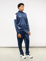 Conjunto deportivo Umbro compuesto por campera de cuello alto con cierre frontal y pantalón de corte recto. La campera presenta bloques de color blanco en los hombros y el logo de la marca bordado en el pecho. Confeccionado en tejido sintético con acabado satinado.