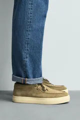 Zapato de cordones con parte superior de piel con acabado en serraje, detalle de bordón en el empeine, horma redonda y suela a contraste.