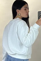Buzo de cuello redondo y manga larga, color negro, con diseño de pequeños puntos brillantes distribuidos por toda la prenda. Presenta puños y ruedo acanalados.