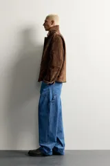 Parka de piel marrón tipo gamuza con cuello solapa, manga larga con puños de botones a presión y múltiples bolsillos de plastrón con solapa en el pecho y la cadera. Cierre frontal de cremallera oculta con solapa.
