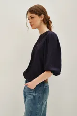 Camisa de color azul marino con mangas tres cuartos abullonadas y puños elásticos. Presenta un diseño con paneles de encaje negro en el frente y cuello redondo.