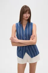 Chaleco color beige claro, sin mangas, con escote en V profundo y cierre frontal asimétrico con botones.