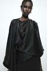 Blusa negra de satén con escote fluido, diseño drapeado en el frente y mangas largas anchas. Presenta un bajo asimétrico y una caída suave y elegante.