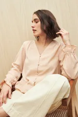 Camisa negra de manga larga con escote en V y botones forrados al tono en el frente. Destaca por su textura sutil y por el detalle de frunces con volados en la parte inferior.