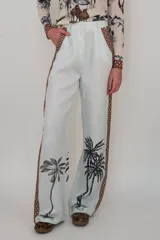 Pantalón de lino color celeste con estampado de palmeras en la parte inferior de las piernas y detalles de guarda pampa en color camel en los laterales. Tiene pretina y bolsillos.