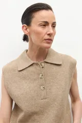 Chaleco de punto color tostado melange, con cuello polo y abotonadura frontal de tres botones. Sin mangas.