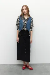 Maxifalda negra de pana con botones metálicos al frente y cuatro bolsillos, dos de ellos con solapa.