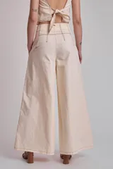 Pantalón marrón de corte palazzo, tiro alto, con pliegues frontales y pespuntes blancos decorativos.