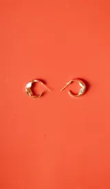 Par de aros tipo argolla pequeños, de color dorado con diseño irregular y acabado brillante.
