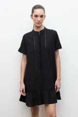 Vestido corto negro de corte amplio, con cuello mao, mangas cortas con volados y detalles de vainillas verticales en el frente. Cuenta con un volante fruncido en el ruedo.