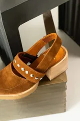 Zapatos tipo zueco de gamuza negra con punta fina y tira sobre el empeine decorada con tachas metálicas plateadas. Posee taco cuadrado de madera y suela con plataforma.