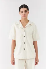 Conjunto de dos piezas color blanco off-white, compuesto por una camisa de manga corta con cuello camisero y bolsillos frontales, y un pantalón largo de corte recto y holgado.