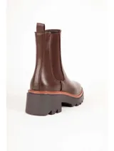 Bota tipo Chelsea de color negro, con elásticos laterales, suela track y taco cuadrado con detalle en tono marrón.