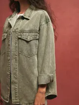 Sobrecamisa verde grisáceo de denim con cuello camisero, cierre frontal con botones, bolsillos con solapa en el pecho y mangas largas con puños abotonados.
