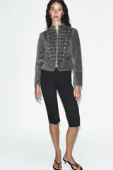 Chaqueta entallada de terciopelo color gris con efecto acid wash, cuello subido, manga larga y cierre frontal con ganchos metálicos. Presenta detalles de pasamanería con falsos botones en el delantero de inspiración militar.