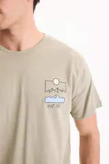 Remera verde claro de corte regular, con manga corta y estampa en la espalda que representa un paisaje de montañas, sol y una ola con la inscripción "est.96".