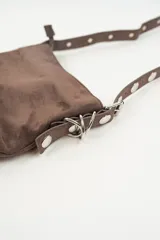Cartera de hombro color marrón, con textura de gamuza, cierre de cremallera y detalle de argollas metálicas en el lateral.