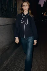 Blusa de color negro con cuello solapa, lazo frontal y manga larga. Presenta detalles de bordados en color crema en los bordes del cuello, el lazo, la tapeta de botones y los puños. Cierre frontal con botones.
