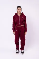 Campera tipo hoodie con cierre frontal, de corte cropped y color bordó. Presenta detalles de líneas blancas en las mangas y un bordado pequeño en el pecho.