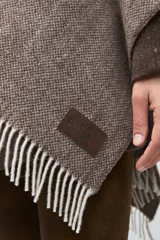 Ruana de lana sin teñir en tonos beige, con textura acanalada y terminaciones con flecos en los bordes.