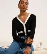 Cardigan de punto blanco con escote en V, botones metalizados, bolsillos falsos, cuello y vista contrastantes en negro, y bajo acanalado.