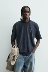 Camiseta relaxed fit color azul marino, con cuello redondo y manga corta. Presenta un estampado combinado a contraste en el delantero y la espalda. El estampado frontal es un texto en cursiva y un dibujo de tres figuras alargadas.