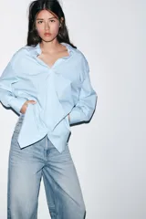 Camisa de corte oversize con estampado de rayas verticales en tonos celeste y blanco. Presenta cuello solapa, escote en pico, manga larga con puños abotonados y un bolsillo de plastrón en el pecho.